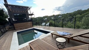 A wooden deck with a swimming pool, lounge chairs, and a pergola with string lights. - Treetop Modern Oasis Lakeway (Austin)