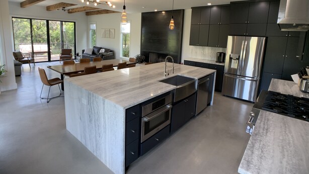 A modern kitchen with a large island, stainless steel appliances, and a dining area with a large table and chairs. - Treetop Modern Oasis Lakeway (Austin)