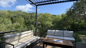A wooden deck with two white sofas and a wooden table, overlooking a forested area. - Treetop Modern Oasis Lakeway (Austin)