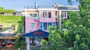 A multi-story building with a pink and white facade, a blue awning with Chinese characters, and a green roof garden. - Xiang Xie Li She Inn (Shenzhen)