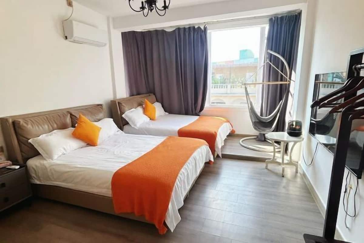 Quarto de hotel com duas camas, televisão, cadeira e varanda com cortinas.