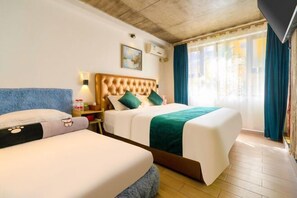 A hotel room with two beds, a large window with curtains, a painting on the wall, and a ceiling with exposed beams.