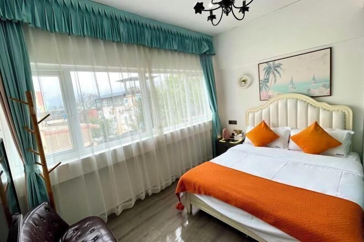 A bedroom with a bed, curtains, a painting, and a nightstand.