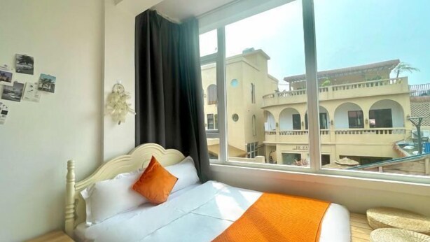A hotel room with a bed, a window with a view of buildings, and a wall with pictures. - Xiang Xie Li She Inn (Shenzhen)