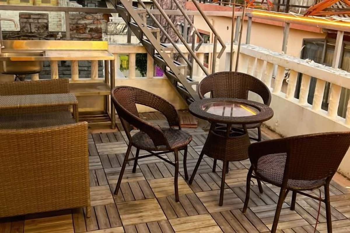 Um deck de madeira com móveis de vime, incluindo cadeiras e uma mesa, com vista para um edifício com uma escadaria.