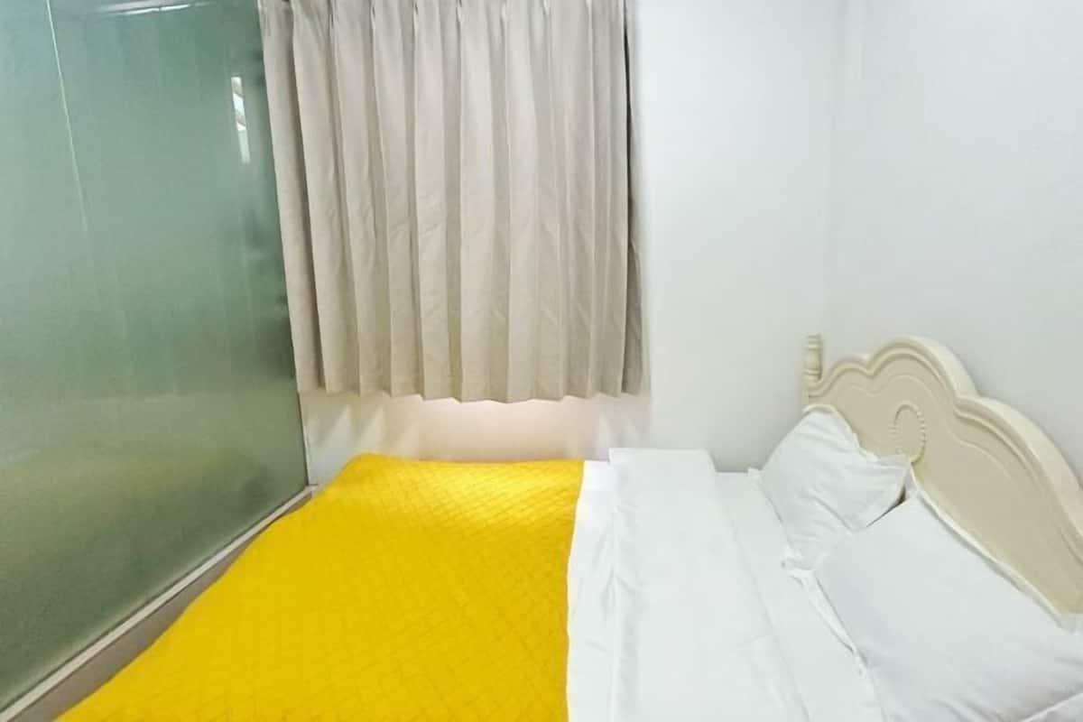 Quarto com uma cama, cortinas brancas e um painel de vidro.