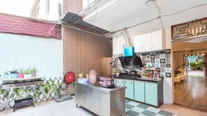 A compact kitchen with a stainless steel counter, a microwave, and a sink. There are cabinets with decorative items and a small table with potted plants. - Xiang Xie Li She Inn (Shenzhen)