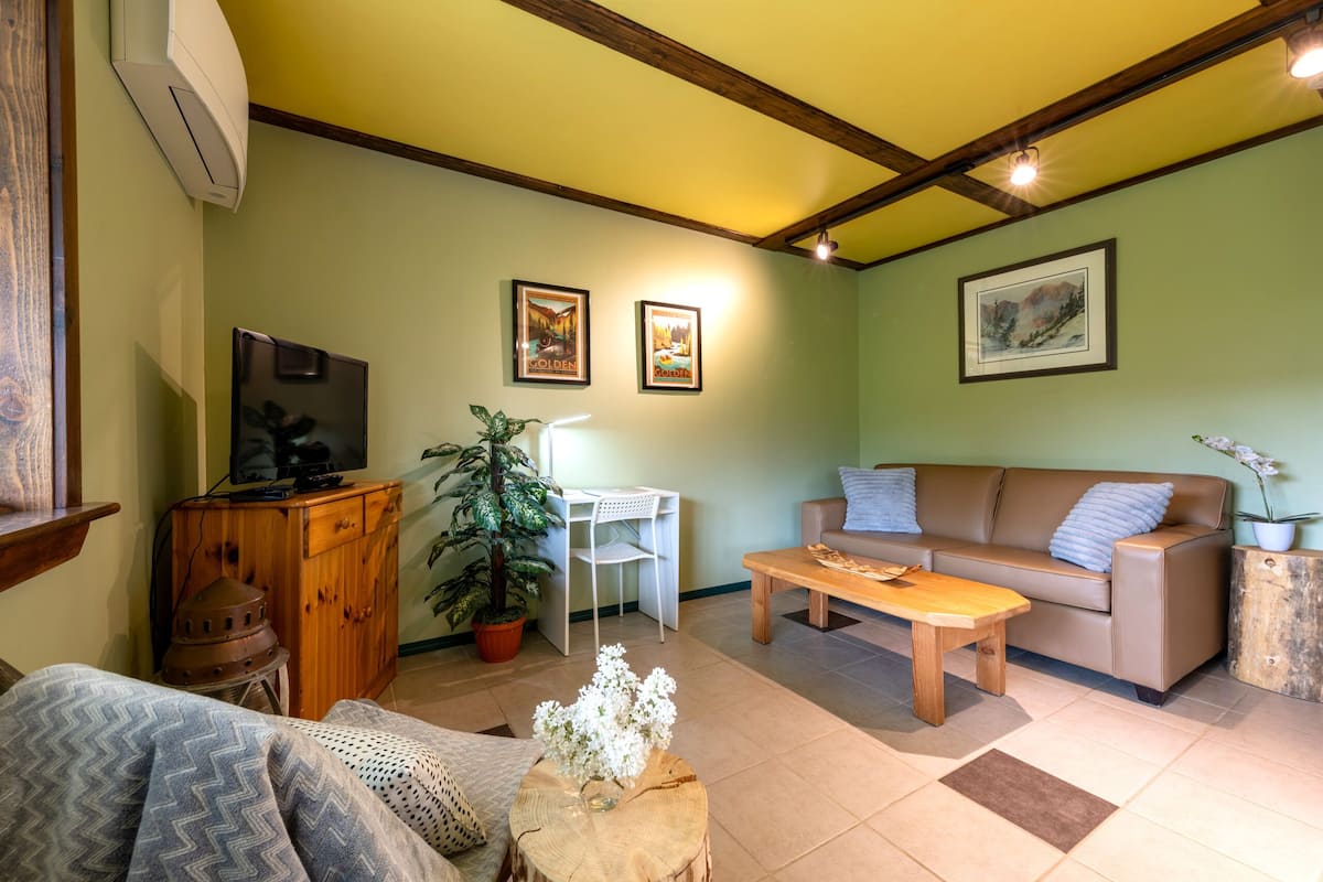 Una sala de estar con sofá, mesa de centro, televisor y plantas decorativas.