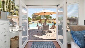 Una stanza con una porta scorrevole in vetro che dà su un patio esterno con piscina, sedie e ombrelloni.