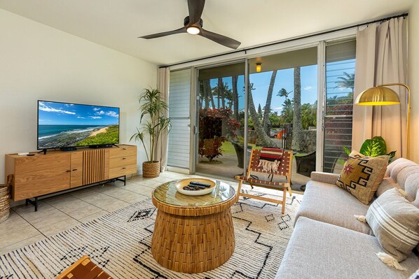 A modern living room with a large TV, a round wooden coffee table, a sofa, and a chair. - Paia Surf Condo (Paia)
