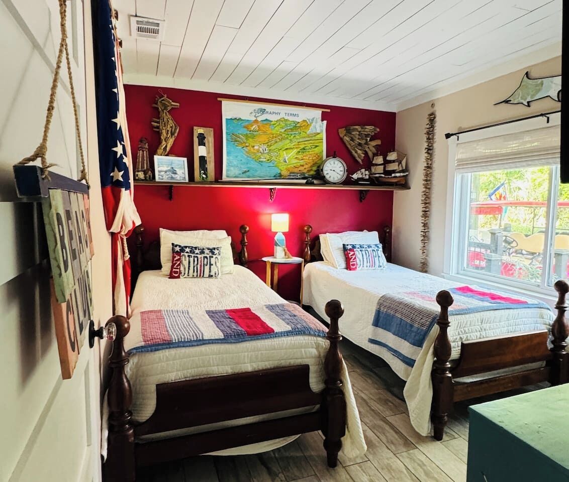 A bedroom with two beds, a red wall, a map, and a window with a view.