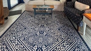 Ein gemütliches Wohnzimmer mit Holzbalkendecke, einem weißen Sofa, einem gemusterten Teppich und einer blauen Akzentwand.
