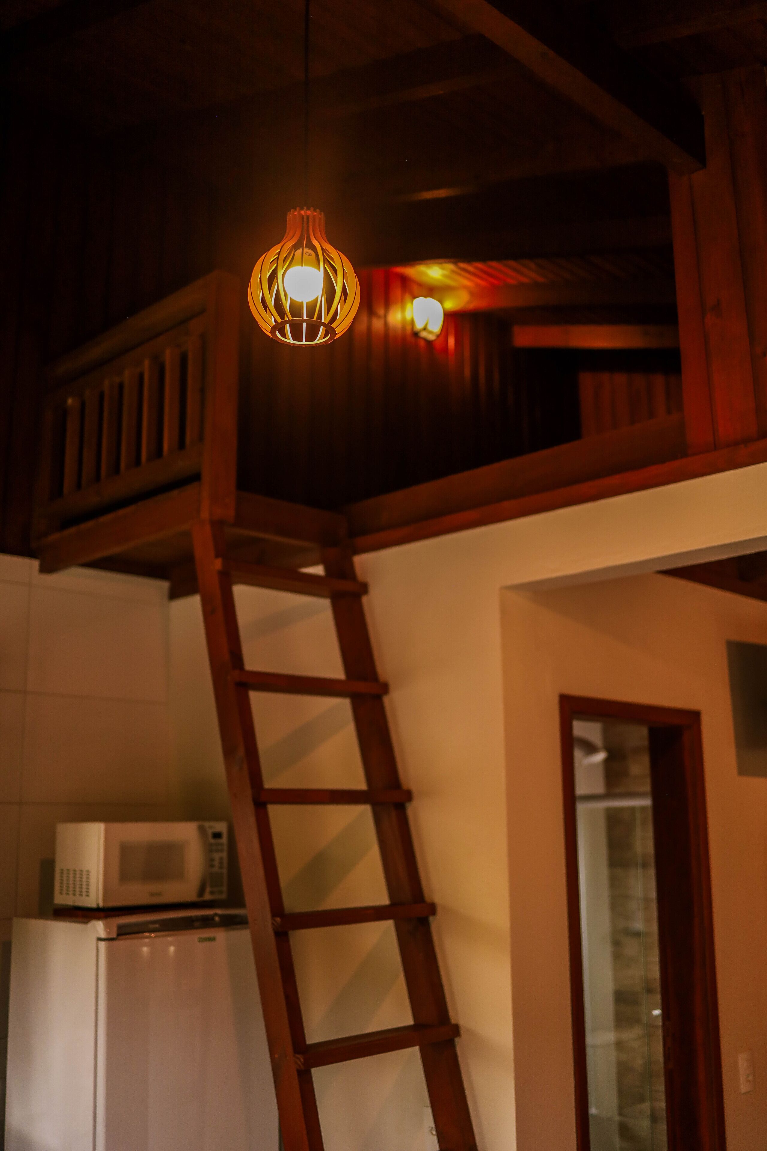 Een houten ladder die leidt naar een hoger gelegen zolderruimte met een hanglamp.