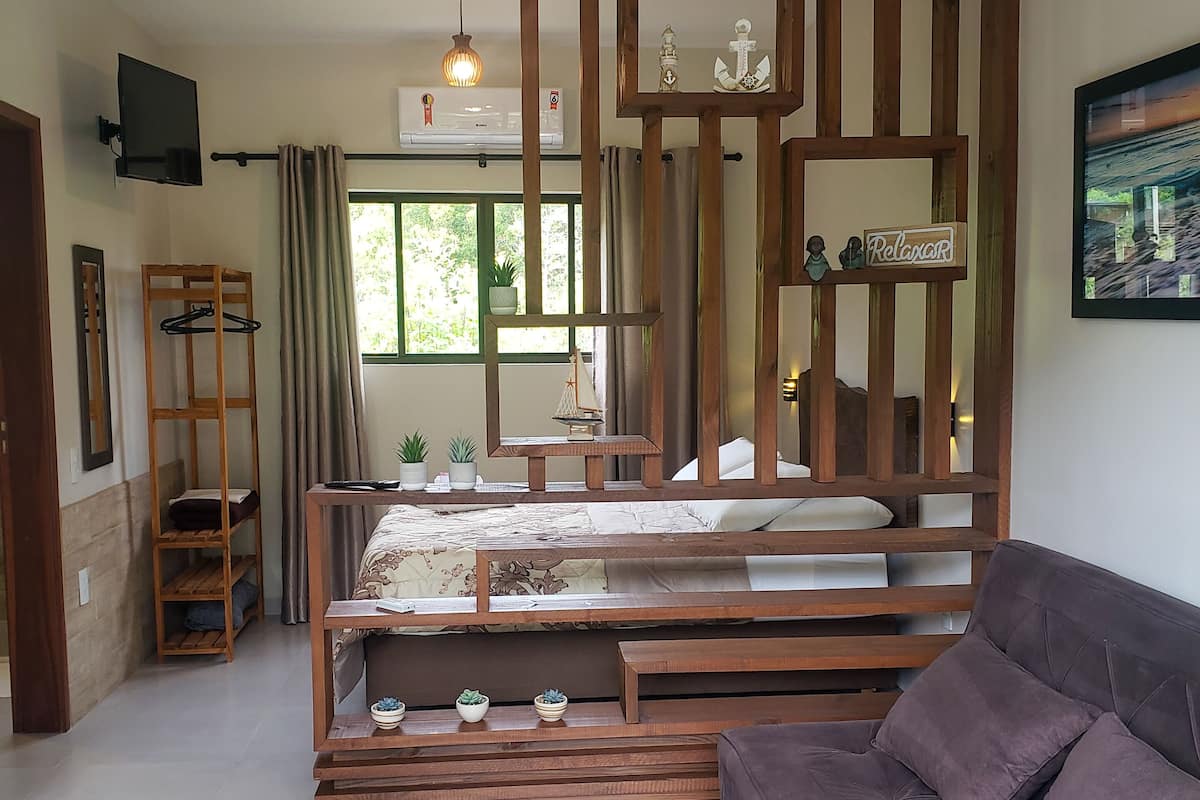 A modern bedroom with a bed, a wooden bench, a sofa, and a TV.