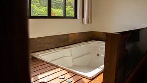 A bathroom with a wooden floor, a bathtub, and a window with a view of greenery. - Pousada Rosa Maria (Imbituba)