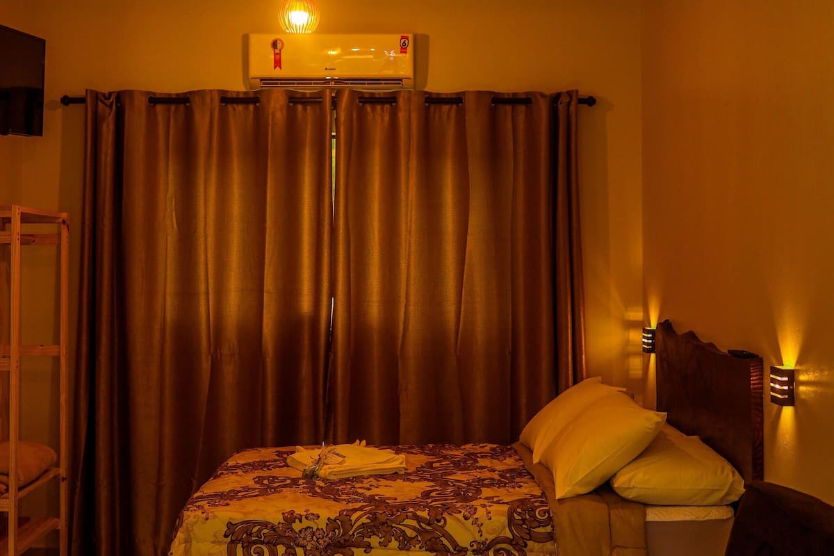 A hotel room with a bed, a sofa, a standing shelf, and an air conditioning unit.