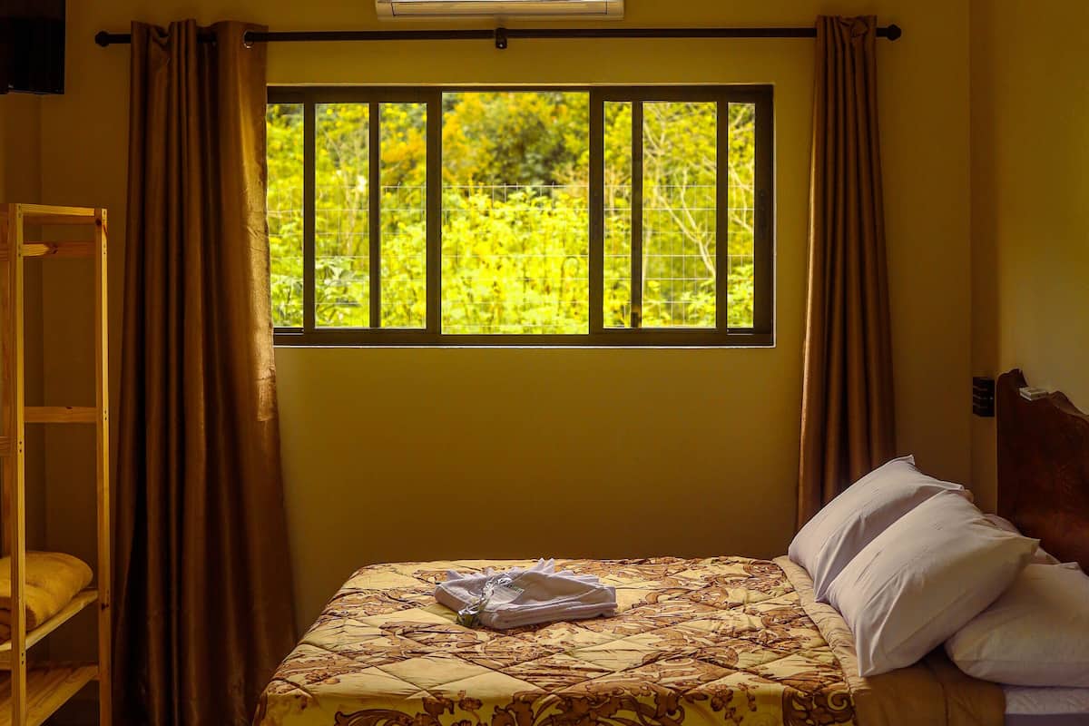 A bedroom with a bed, a window with curtains, a ceiling fan, and an air conditioning unit.