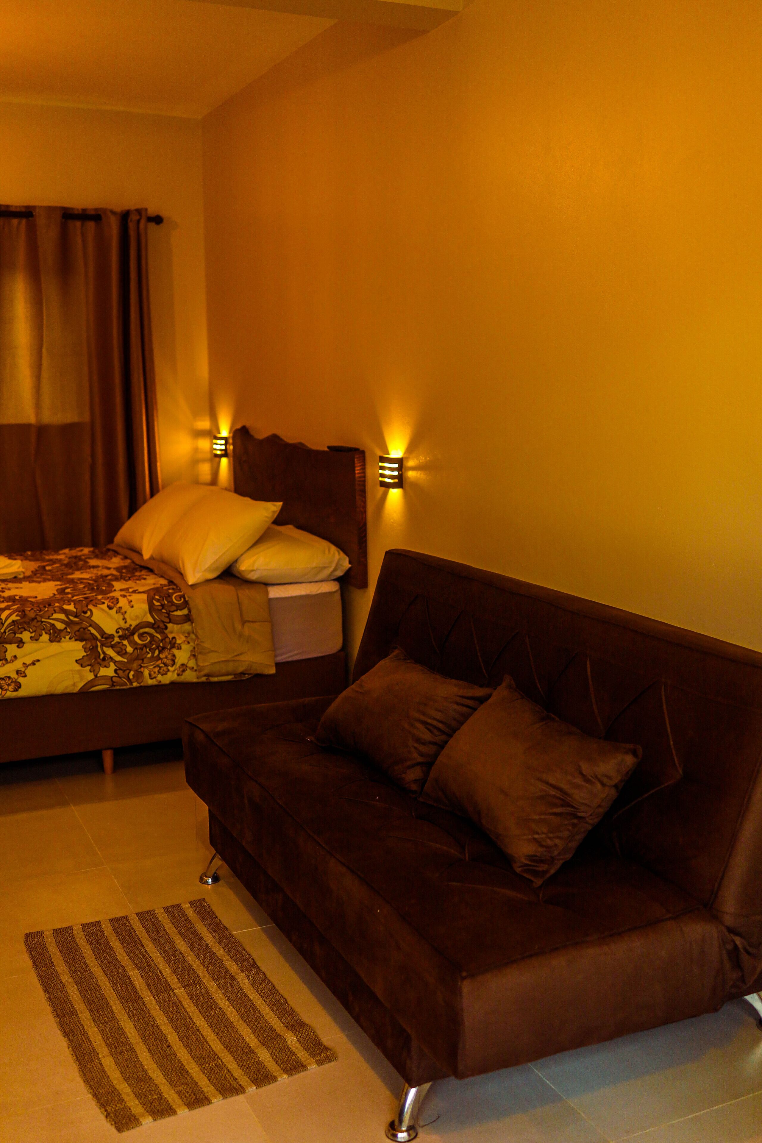 Une chambre à coucher avec un lit, un canapé marron, un tapis à rayures et deux lampes fixées au mur.