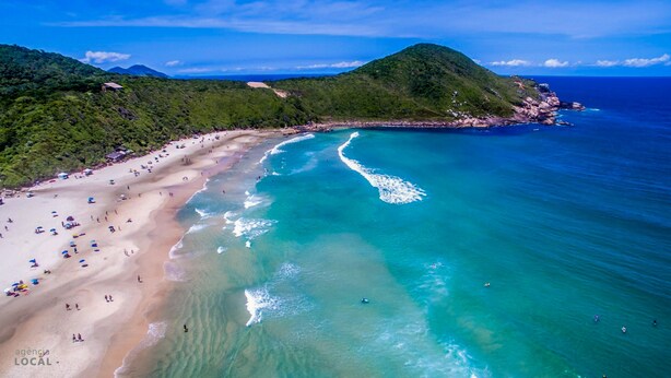 A beach with clear turquoise waters, a sandy shore, and a mountainous backdrop. - Pousada Rosa Maria (Imbituba)