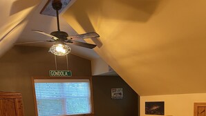 A bedroom with a wooden bed, a ceiling fan, a window with blinds, and a wall-mounted sign. - Rush Hollow Hideaway (Lake George)