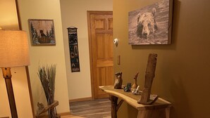 A hallway with wooden flooring, a wooden table with decorative items, a lamp, and wall art. - Rush Hollow Hideaway (Lake George)
