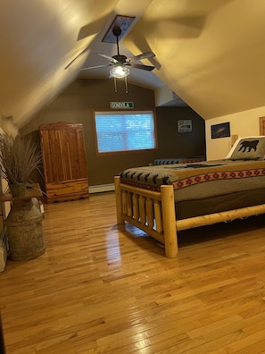 Cozy attic bedroom with a wooden bed, ceiling fan, and potted plant.