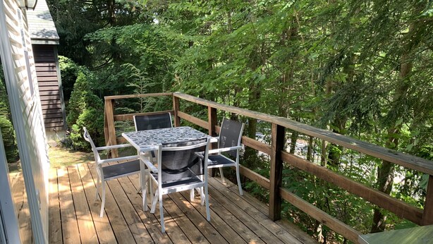 A wooden deck with a table and chairs, surrounded by lush greenery. - Rush Hollow Hideaway (Lake George)