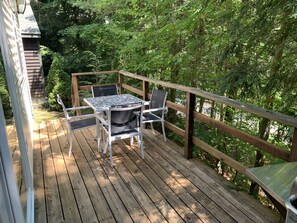 A wooden deck with a table and chairs, surrounded by lush greenery. - Rush Hollow Hideaway (Lake George)