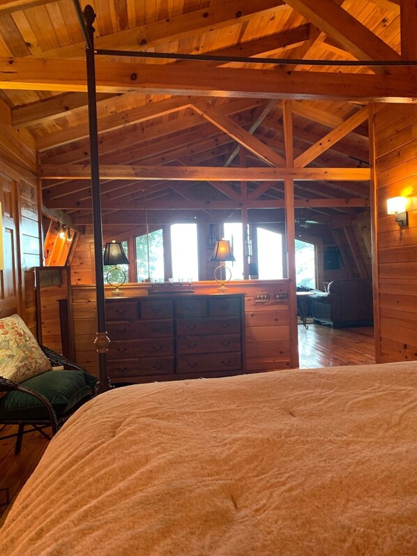 Un dormitorio acogedor en el ático con techo de madera, una cama con colcha, un aparador y una zona de escritorio con lámpara.