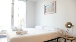 Una cama bien tendida con ropa de cama y toallas blancas, una mesita de noche con lámpara y un cuadro en la pared.
