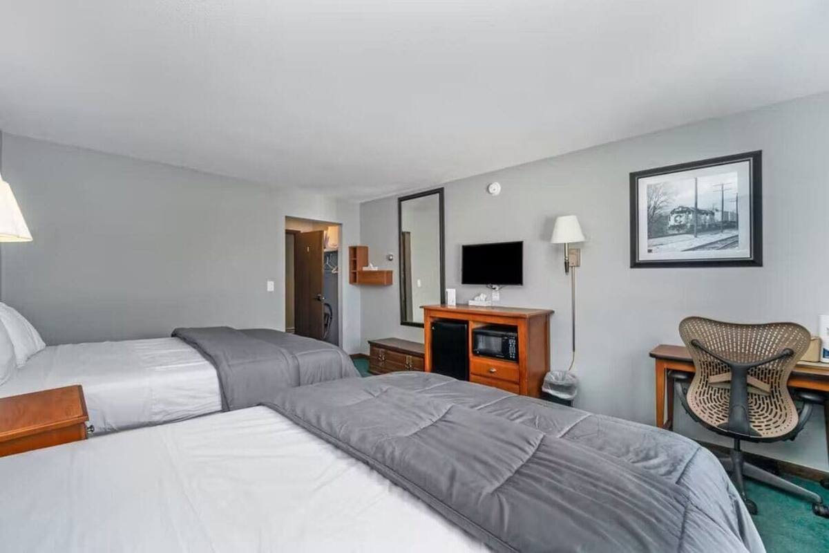 Una habitación de hotel con dos camas, un escritorio, una silla, un televisor y un espejo.