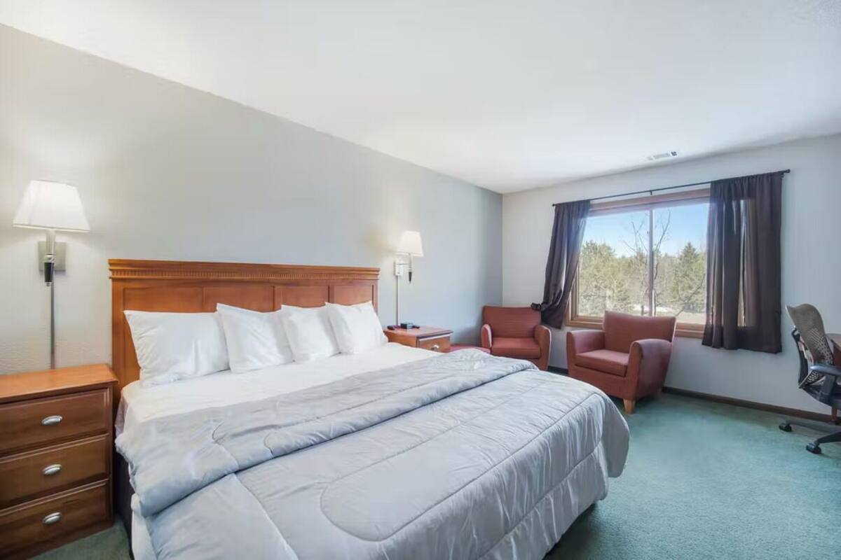 Una habitación de hotel con una cama grande, dos sillones, un escritorio y una ventana con cortinas.