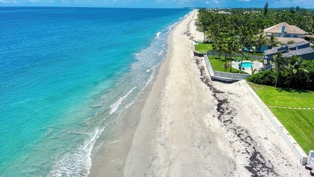 Una playa con vista despejada al océano, piscina y una casa con jardín.