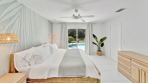 Un dormitorio moderno con una cama grande, un ventilador de techo, vista a una piscina y un aparador de madera.