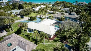 Zona residencial con una casa grande que tiene piscina, rodeada de palmeras y vista al océano.