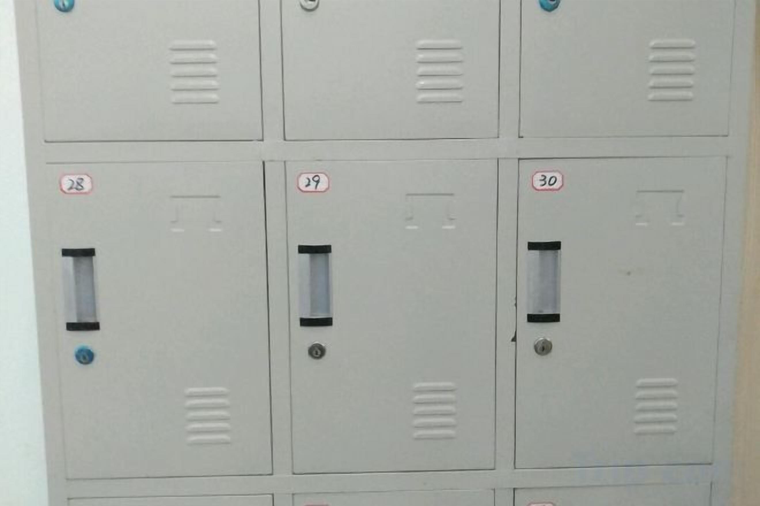 Una fila di armadietti metallici grigi con i numeri 28, 29 e 30 ben visibili.