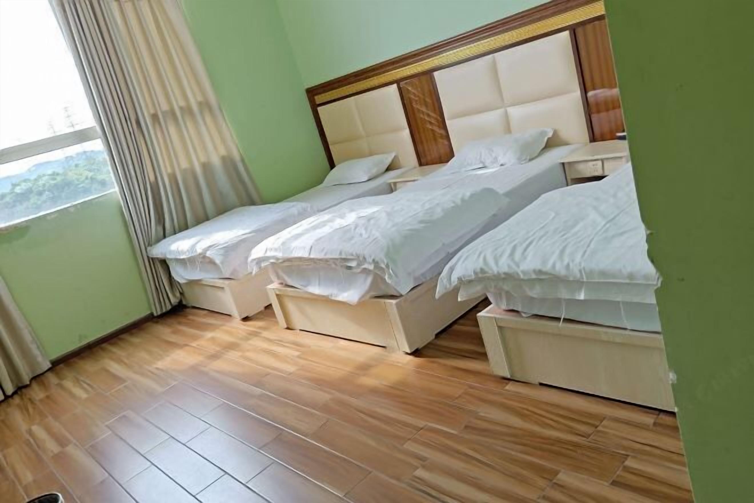 A hotel room with two beds, a window with curtains, and a wooden floor.