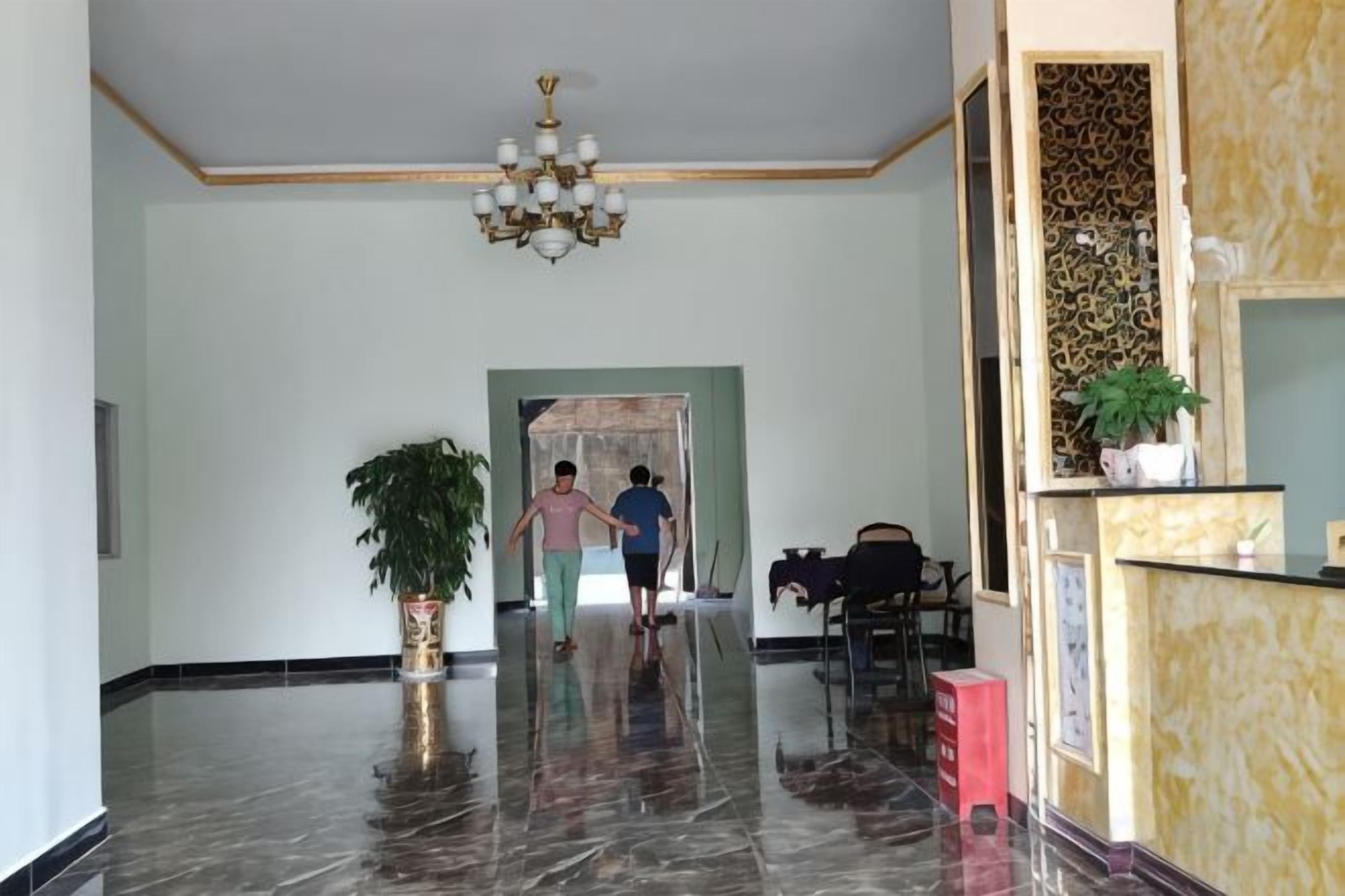 A spacious lobby with a marble floor, a chandelier, a reception desk, and a potted plant.
