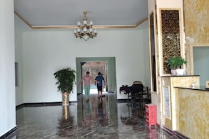 A hotel lobby with a marble floor, a chandelier, a reception desk, and a plant.