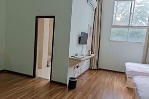 A hotel room with a wooden floor, a bed, a desk with a computer, a window, and a door.