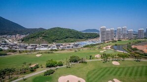 A golf course with a clubhouse, a parking area, and a residential area with high-rise buildings in the background. - Lantian Weekend Vacation Homestay (Yangjiang Hailing Island Poly Silver Beach) (Yangjiang)