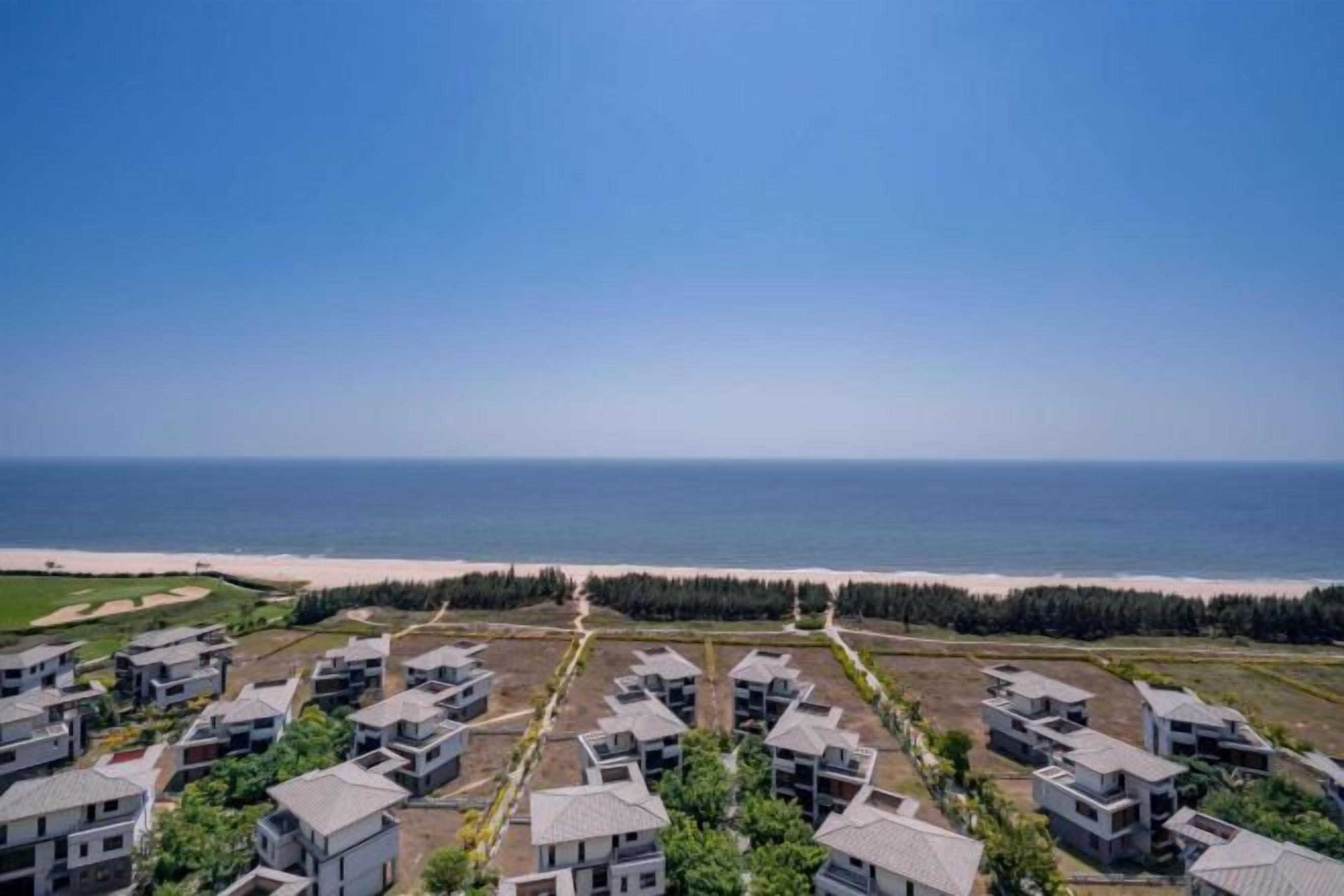 A coastal residential area with modern houses arranged in rows, a beach in the background, and a clear sky.