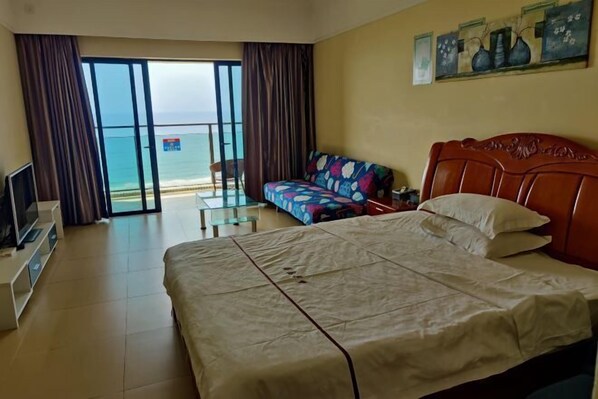 A hotel room with a bed, a sofa, a TV, and a view of the beach through the sliding doors. - Lantian Weekend Vacation Homestay (Yangjiang Hailing Island Poly Silver Beach) (Yangjiang)