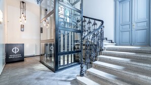 Een modern interieur met een glazen ingang, een trap met sierlijke metalen leuningen, en een bord met de tekst 'REZIDENCE OPELTALOVA'.
