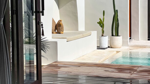 Uma área moderna na piscina com deck de madeira, paredes brancas e plantas em vasos.