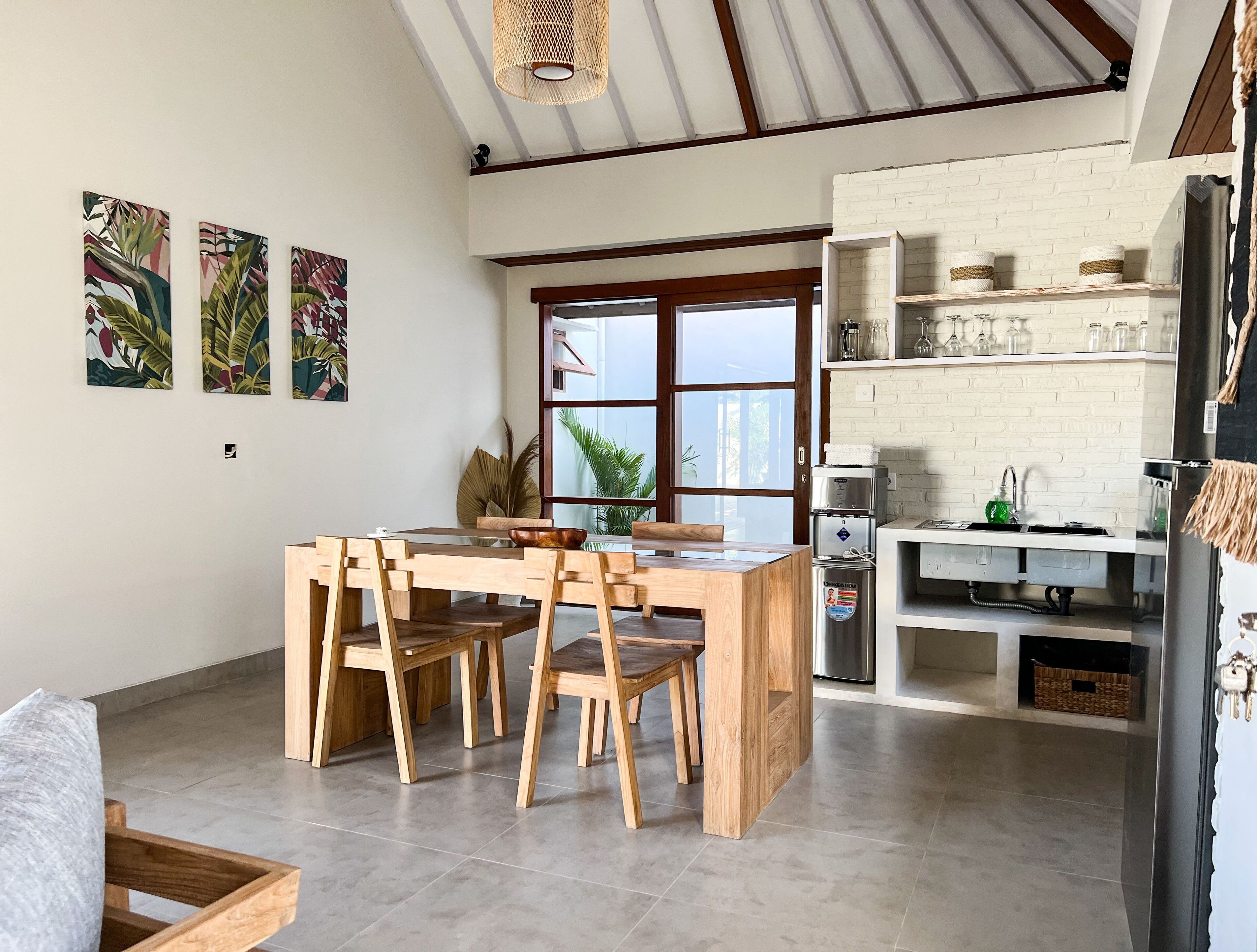 A modern kitchen with a wooden dining table and chairs, a large window, and a white brick wall.
