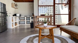 Uma cozinha moderna com geladeira embutida, uma mesa de jantar de madeira com planta em vaso e vista para um prédio residencial através de uma porta de vidro.