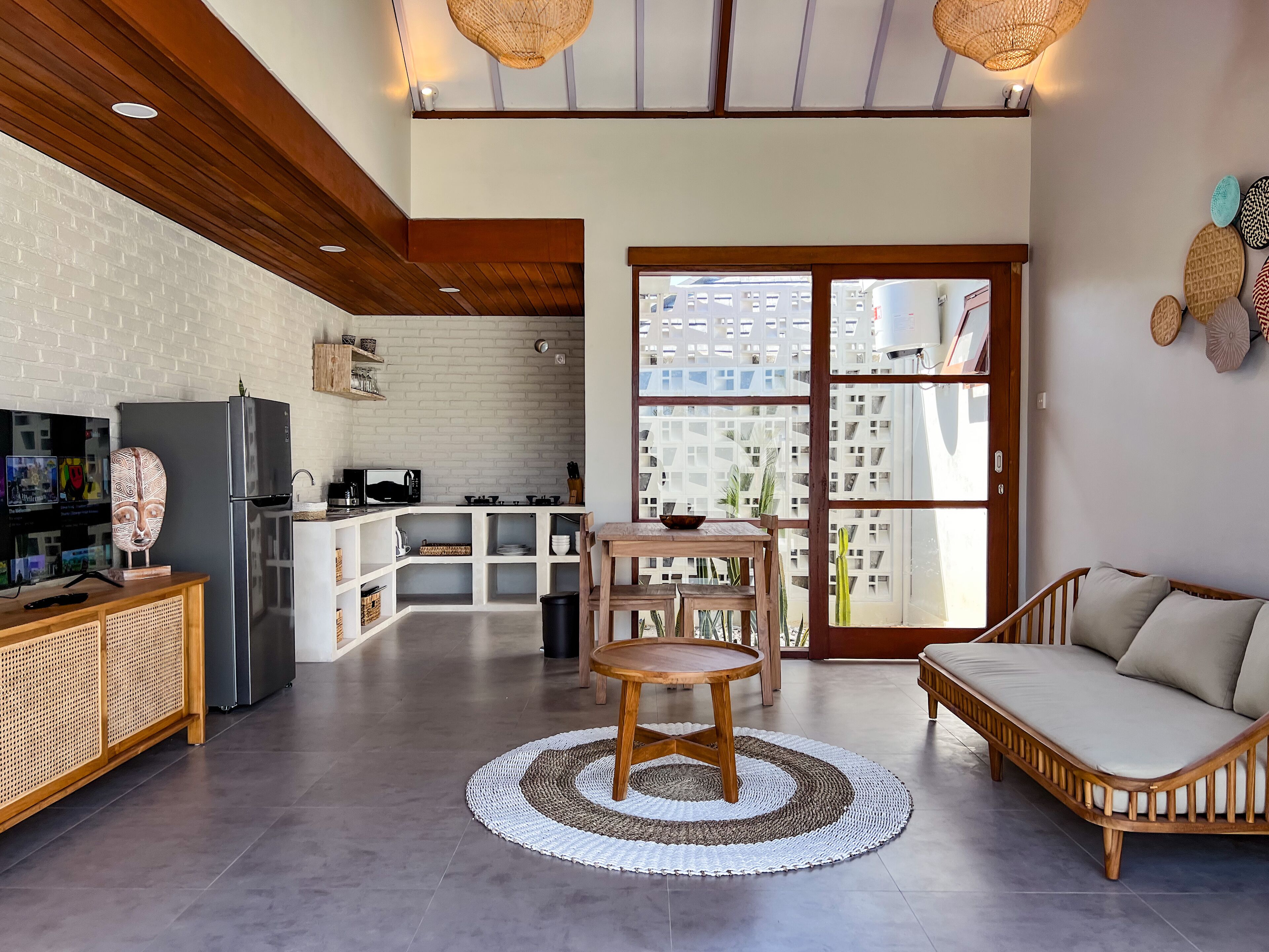A modern kitchen with a refrigerator, microwave, and stove. There is a dining area with a round table and chairs. The room has a large window and a view of buildings outside.