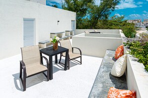 Un patio al aire libre con una mesa y sillas, un pequeño jarrón decorativo y una zona de estar con cojines.