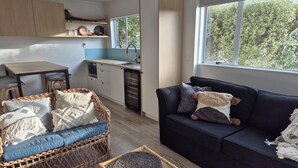 Een ruimtelijk ingerichte leefruimte met kitchenette, eethoek en een comfortabele bank met kussens.